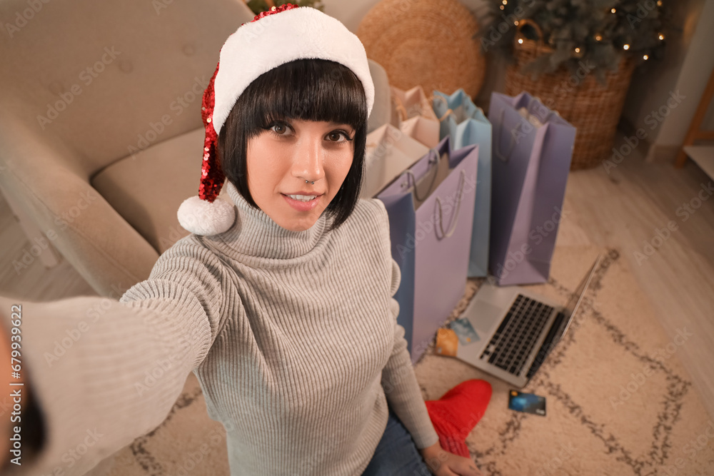 Young woman taking selfie while shopping online for Christmas at home