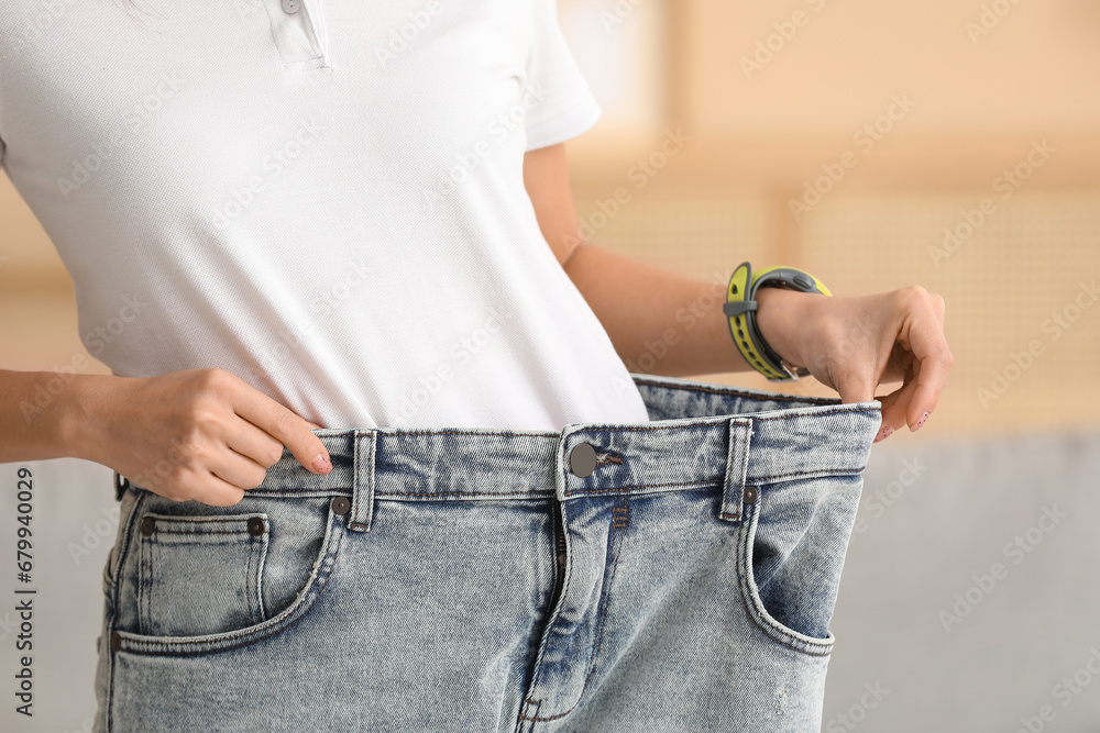 Beautiful young Asian woman in loose jeans at home, closeup. Weight loss concept