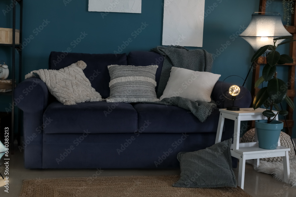 Interior of dark living room with blue sofa and glowing lamps