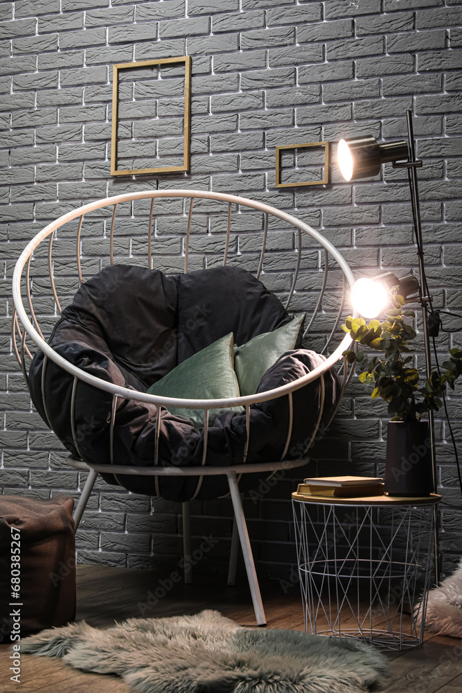 Stylish armchair and glowing lamps on table near grey brick wall