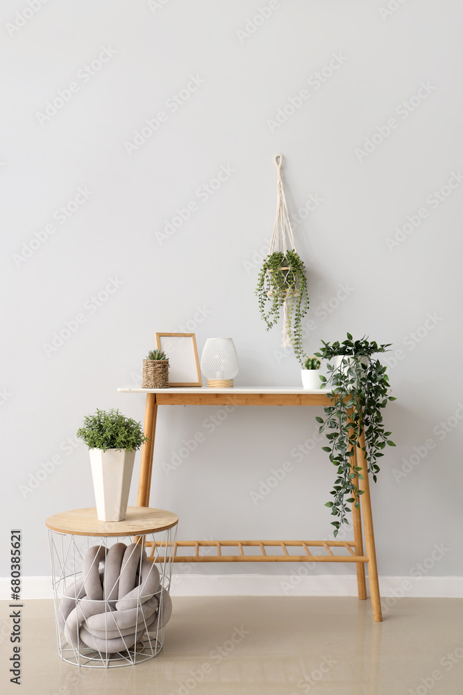 Console table with different houseplants, lantern and empty photo frame near white wall