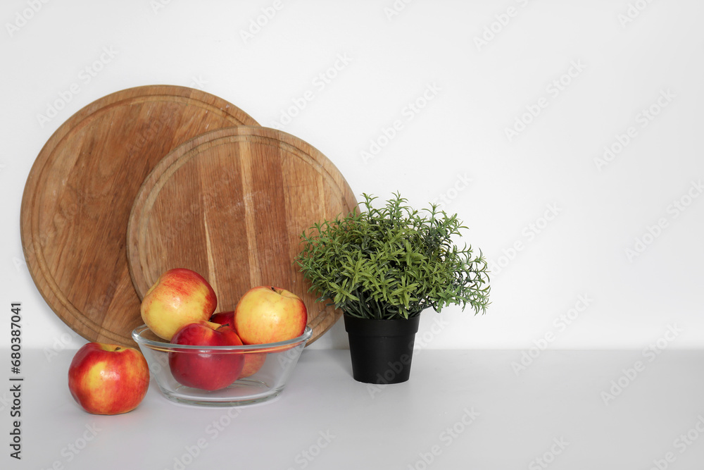 Bowl with apples, houseplant and cutting board on white kitchen counter