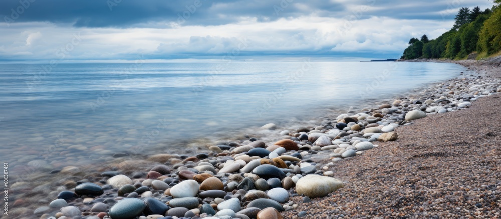 After the storm passed, the grey sky above the Baltic Sea cleared, revealing the tranquil waters gently lapping against the shore, where sand, waves, and stones created a picturesque scene in Poland.