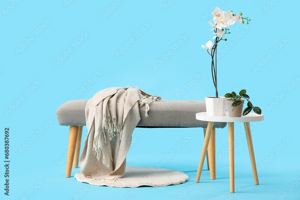 Grey bench and beautiful flowers on coffee table against blue background