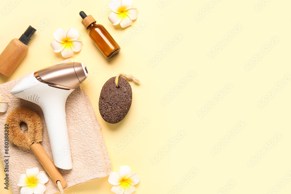 Modern photoepilator with bath supplies, cosmetic products and beautiful flowers on yellow background