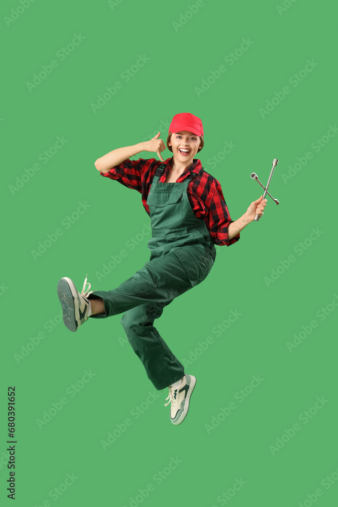 Jumping female worker with cross wrench showing  call me  gesture on green background