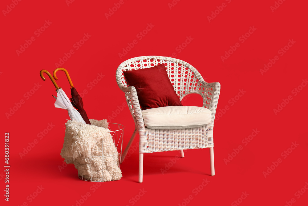 Wicker chair with pillow, basket and blanket on red background