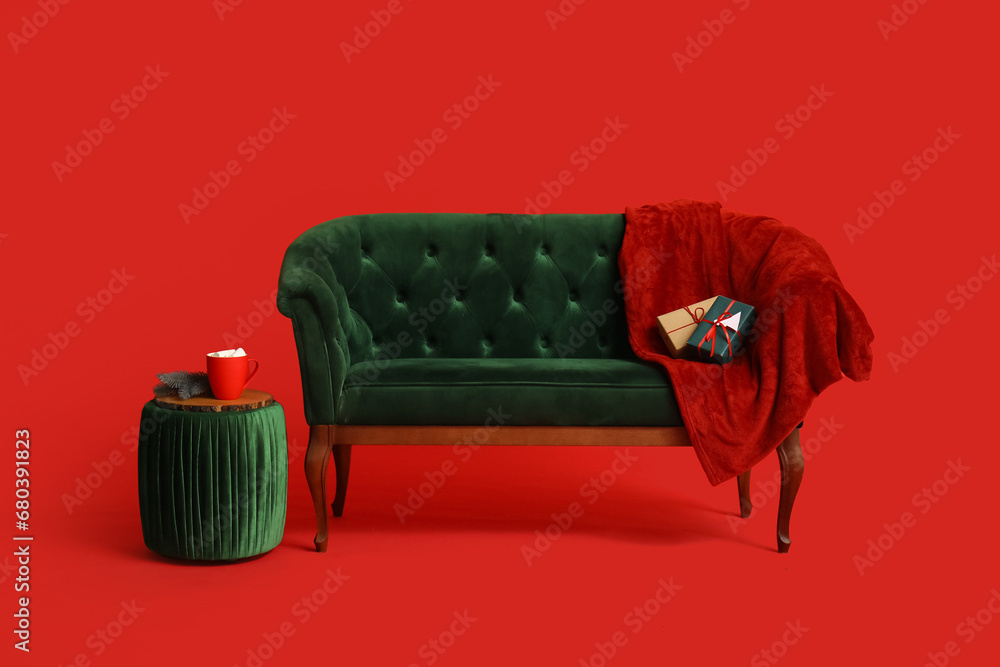 Modern green sofa with blanket and ottoman on red background