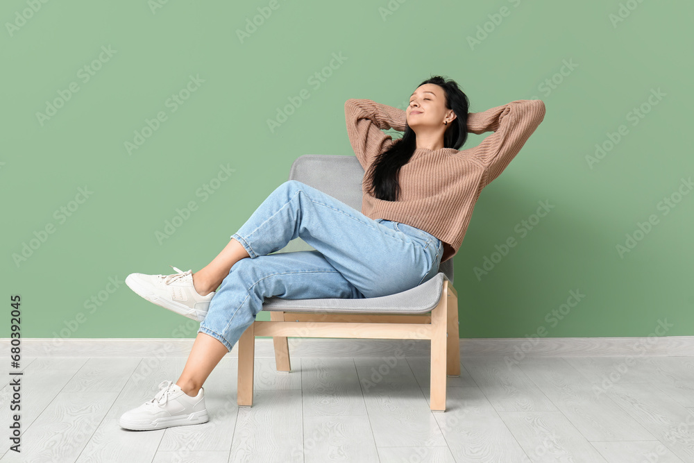 Beautiful young woman resting in comfortable chair near green wall