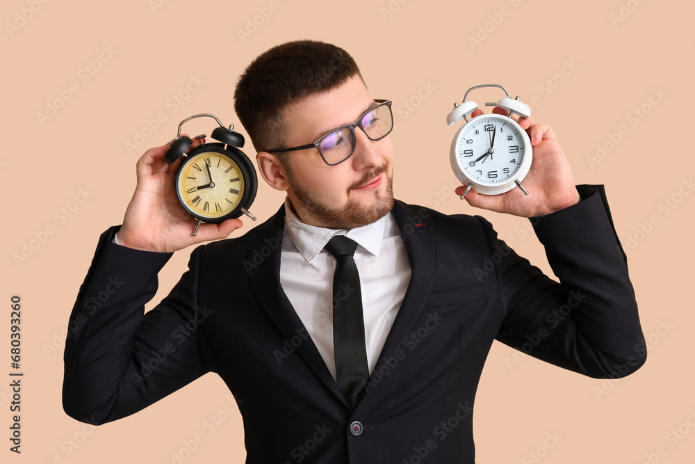 Young businessman with alarm clocks on beige background. Time management concept