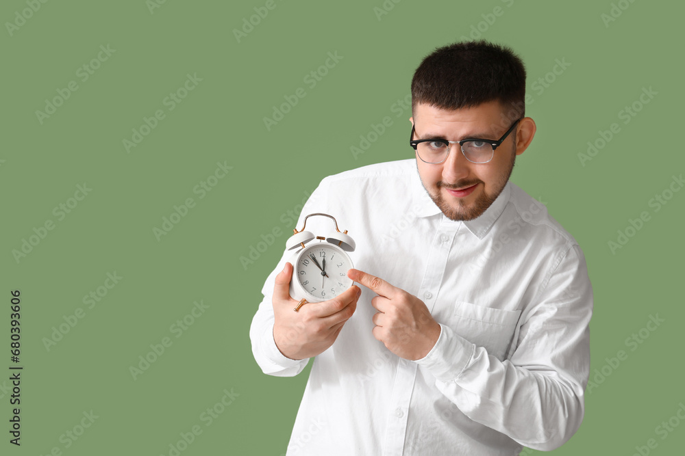 Young happy businessman pointing at alarm clock on green background. Time management concept