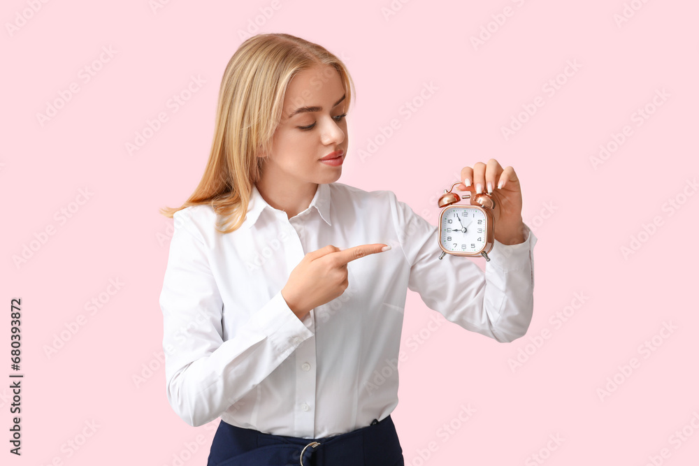 Young businesswoman pointing at alarm clock on pink background. Time management concept