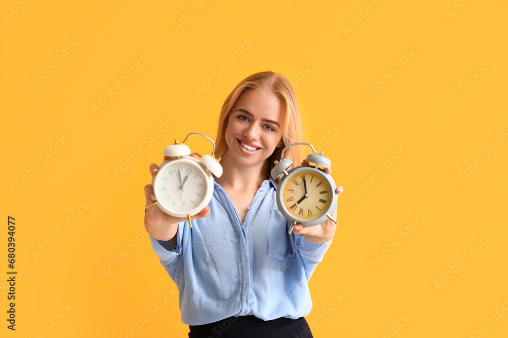 Young happy businesswoman with alarm clocks on yellow background. Time management concept