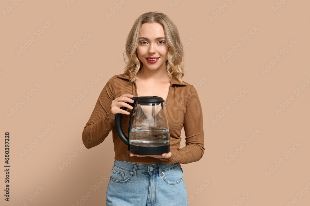 Beautiful young woman with modern electric kettle on beige background