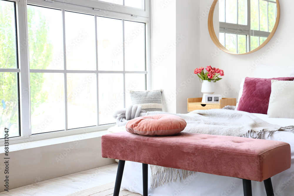 Interior of light bedroom with pink bench and mirror