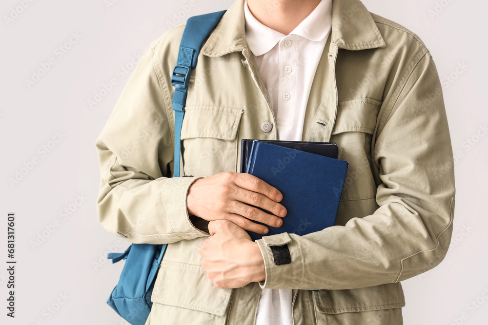 Male student with backpack and books on grey background