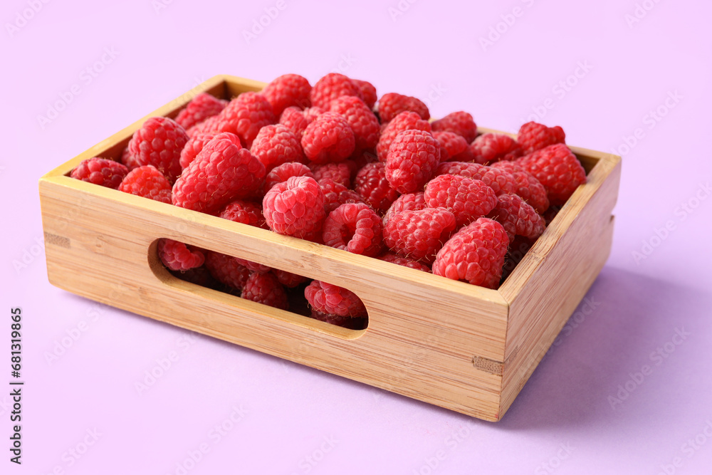 Wooden box with fresh raspberries on lilac background