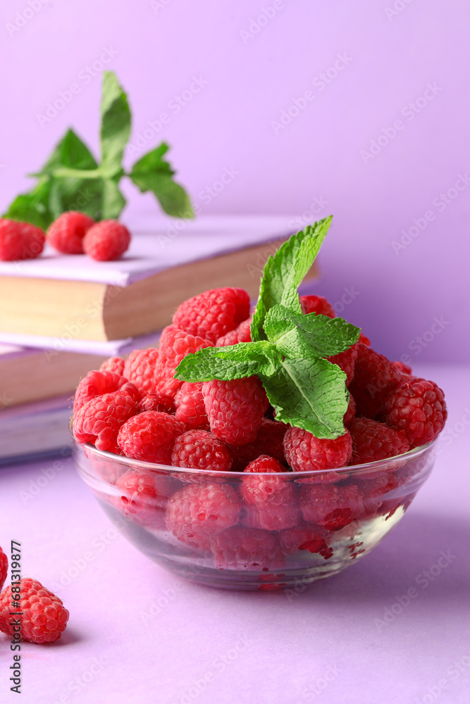 Glass bowl with fresh raspberries and books on lilac background