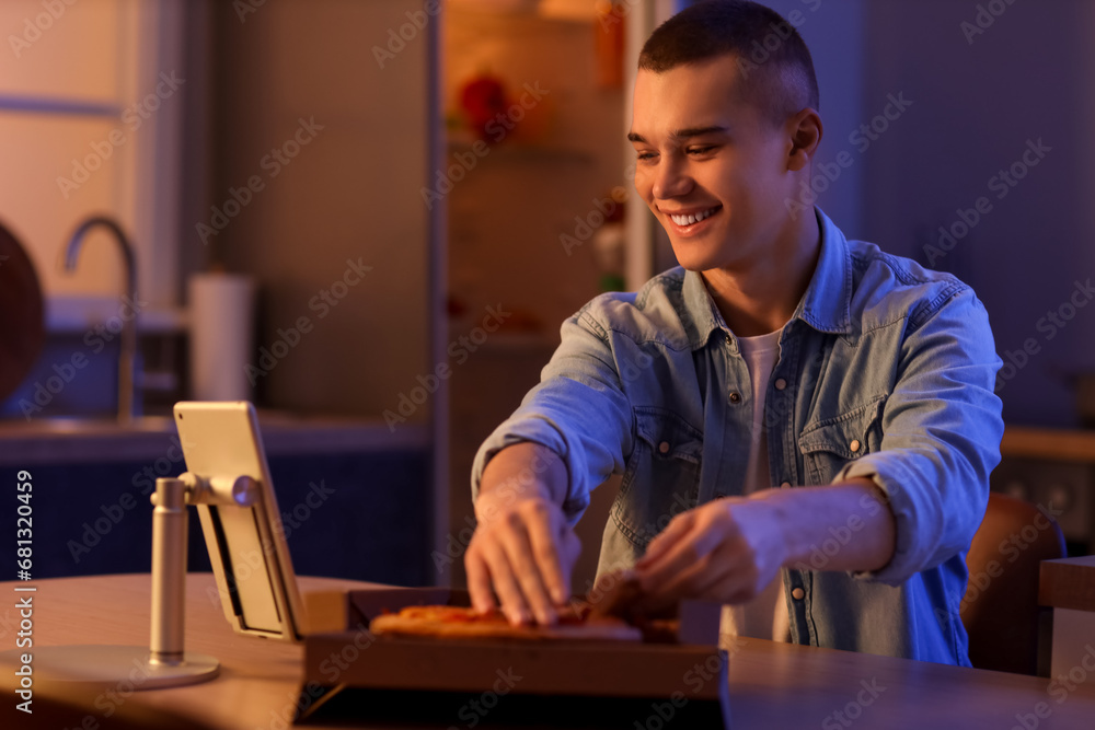 Hungry young man with pizza in kitchen at night