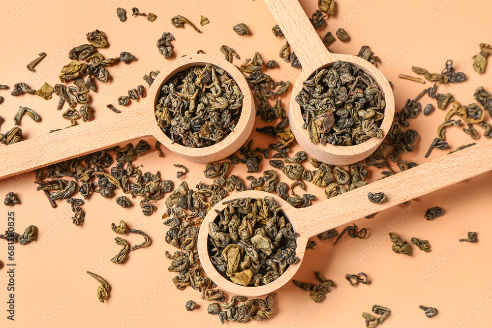 Wooden spoons with dry tea leaves on orange background