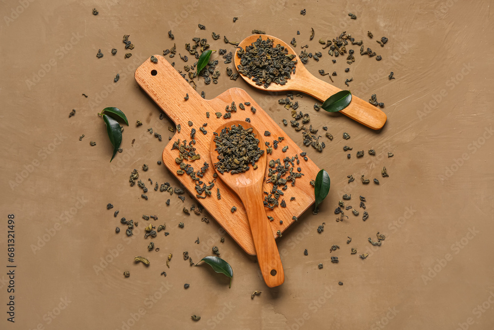 Wooden spoons and board with green tea leaves on brown background