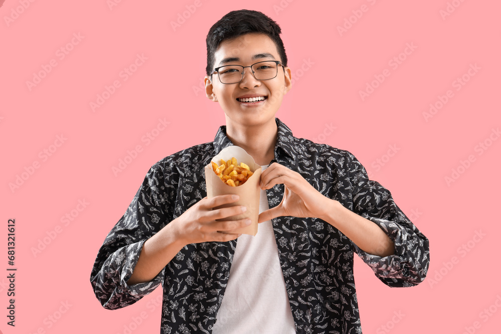 Young Asian man with french fries making heart gesture on pink background