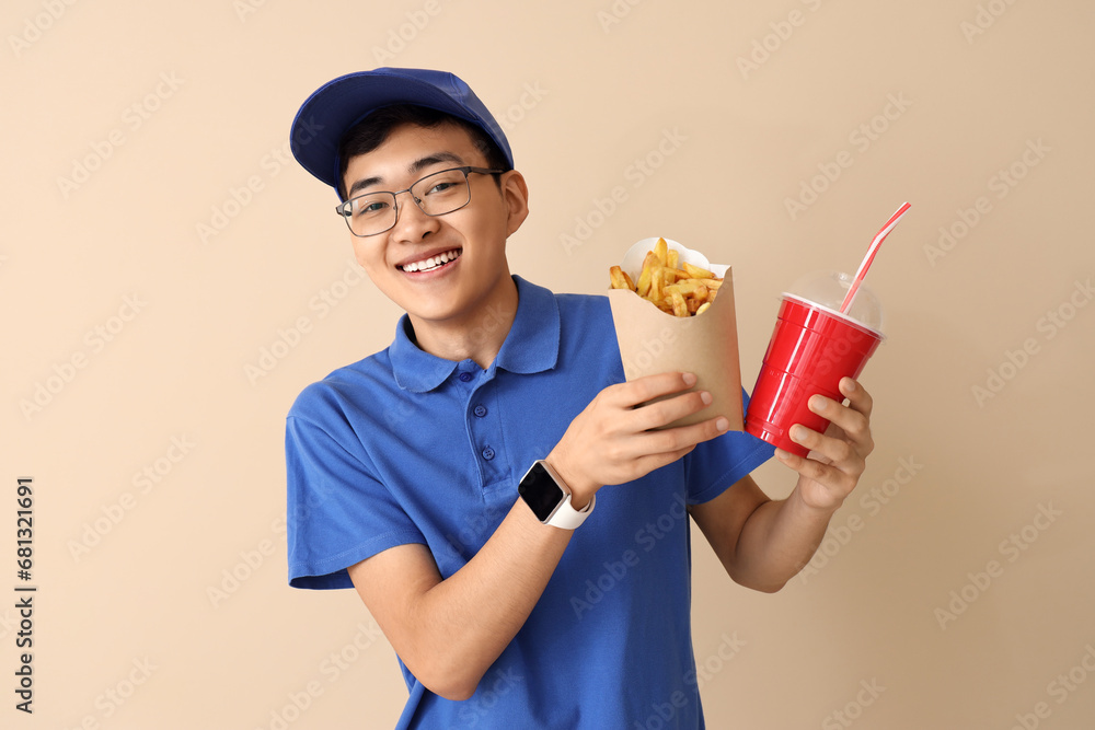 Asian delivery man with french fries and soda on beige background