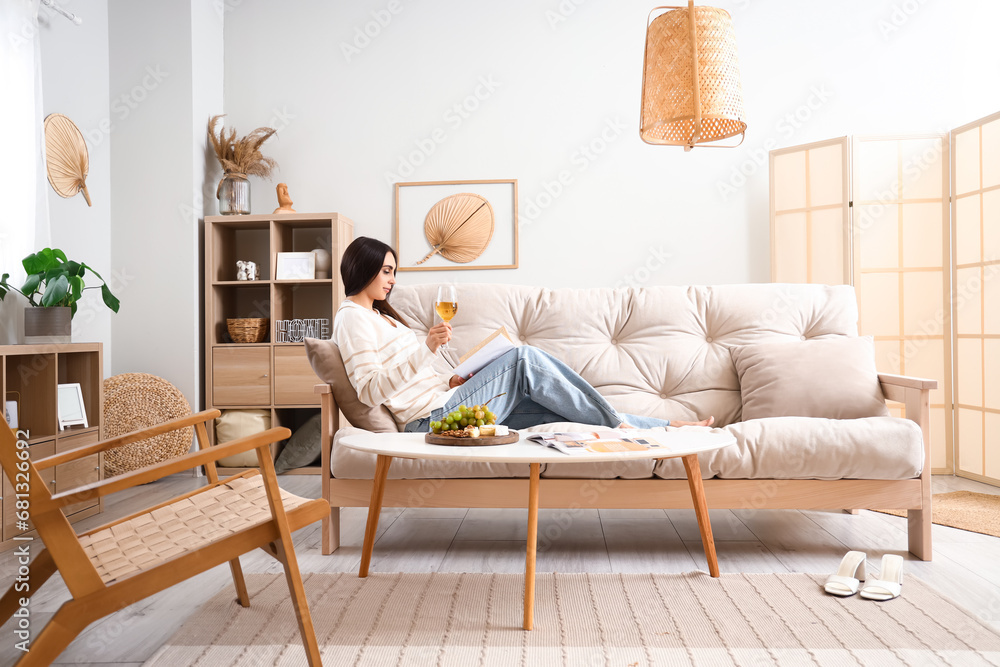 Young woman with glass of wine reading book at home