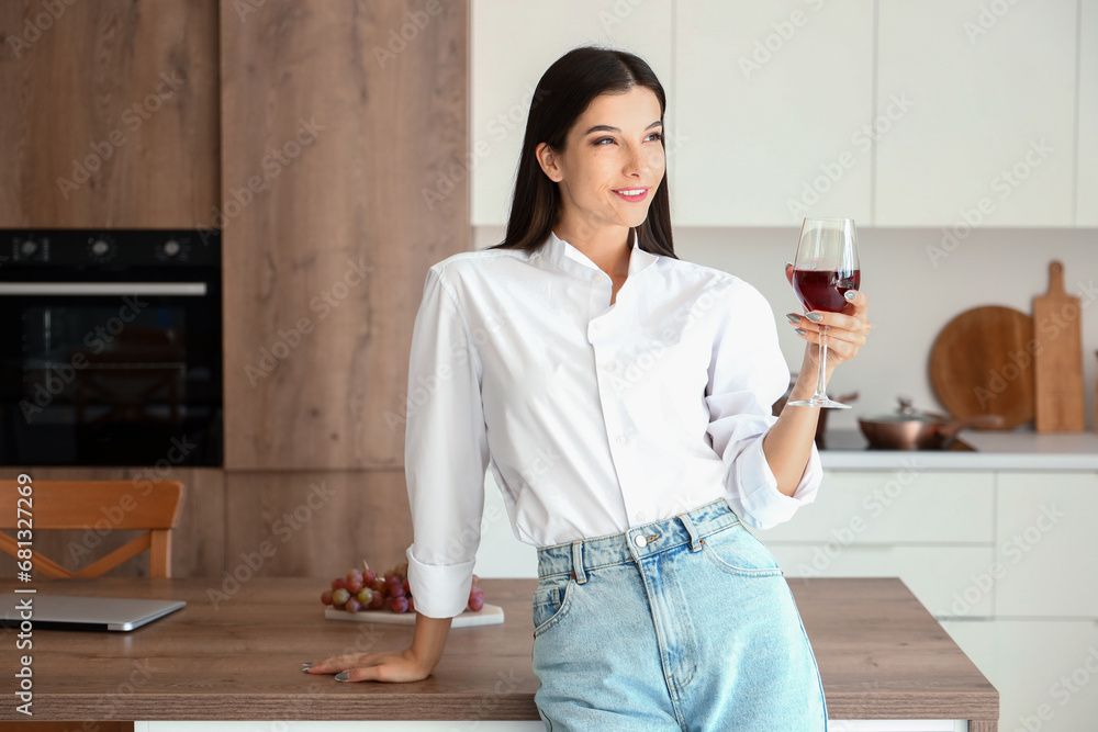 Young woman with glass of wine in kitchen