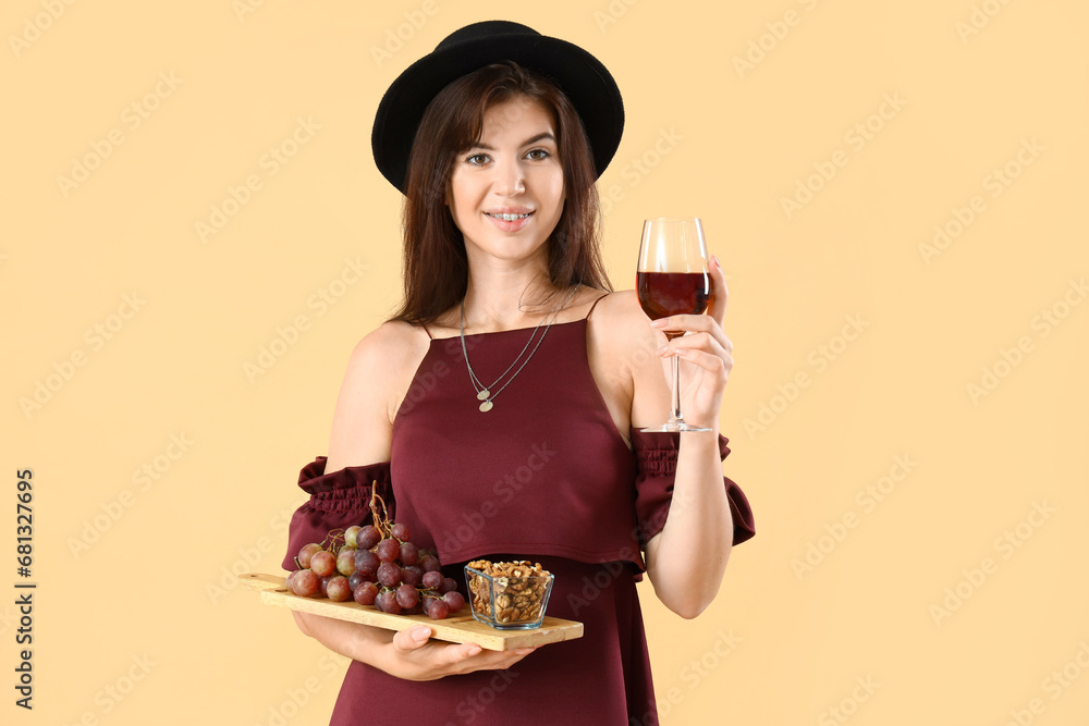 Beautiful young woman with glass of red wine and snacks on beige background