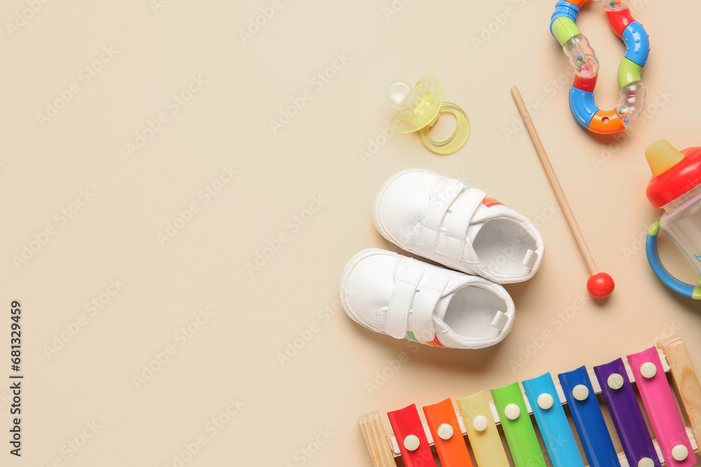 Stylish baby shoes with pacifier and different toys on beige background