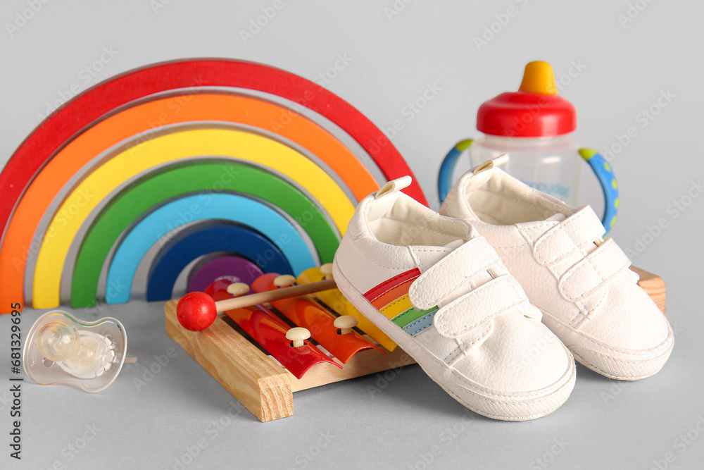 Stylish baby shoes with toys, pacifier and bottle of milk on grey background