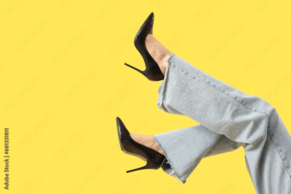 Legs of young woman in stylish black high heels on yellow background