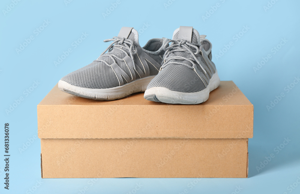 Cardboard box with stylish grey sneakers on blue background