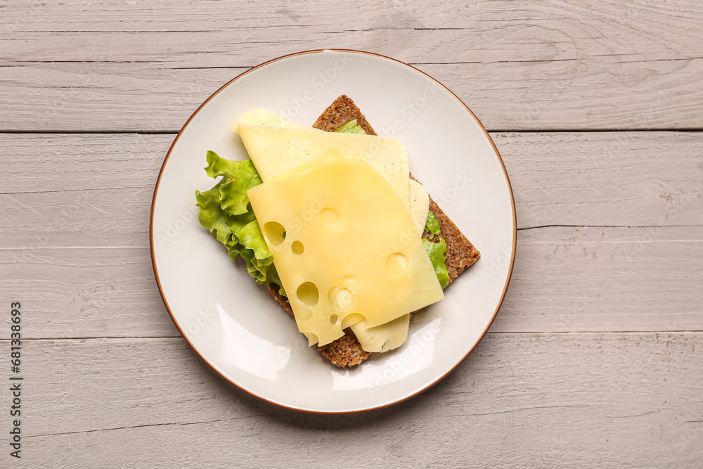 Tasty sandwich with cheese and lettuce in plate on wooden background