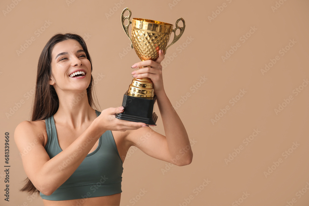 Sporty young woman with gold cup on beige background