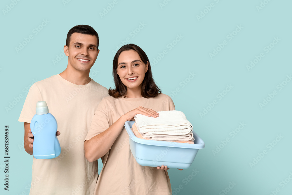 Young couple with laundry basket and bottle of detergent on blue background