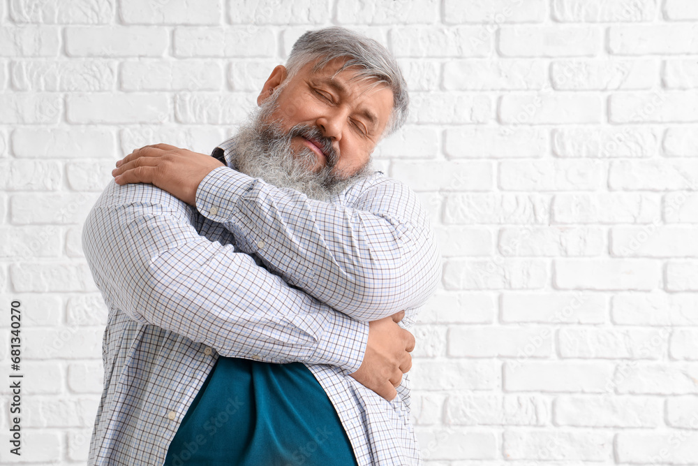 Mature man hugging himself on white brick background