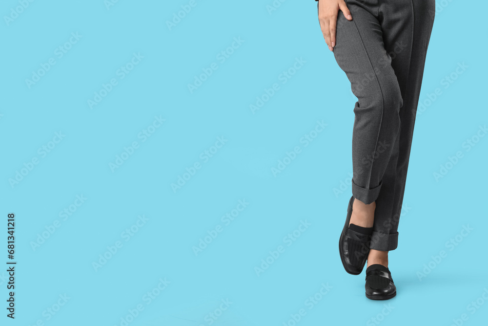 Legs of young woman in stylish black shoes on blue background