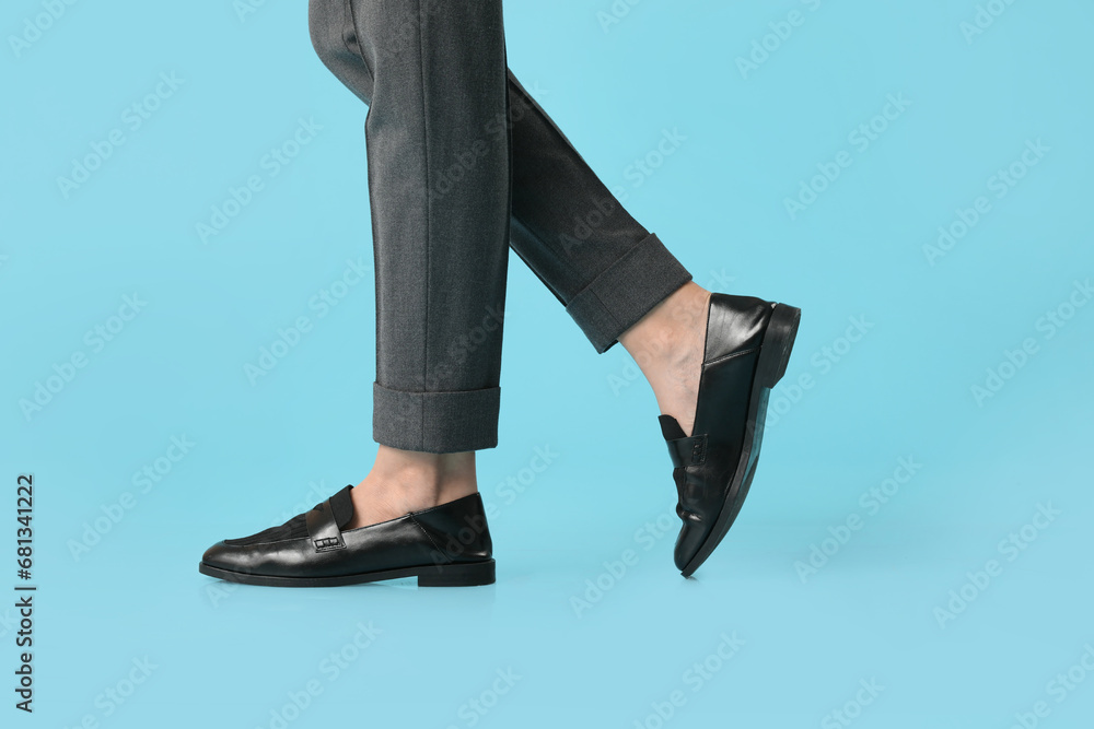 Legs of young woman in stylish black shoes on blue background