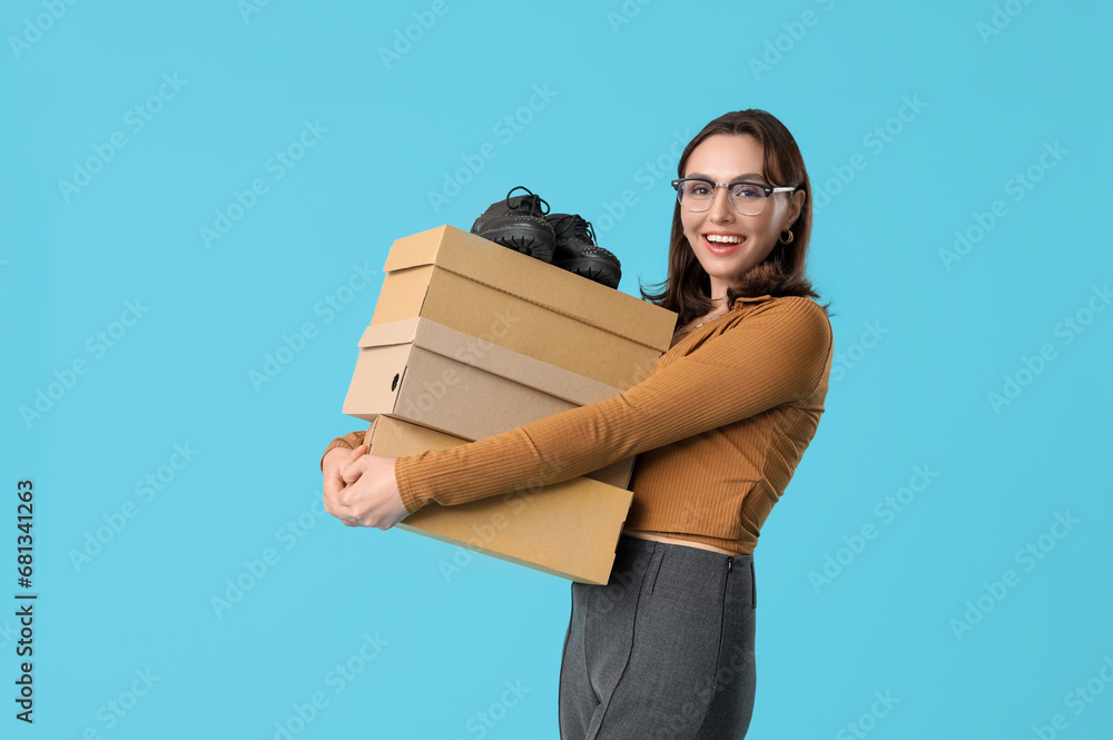 Beautiful young woman holding cardboard boxes with stylish black shoes on blue background