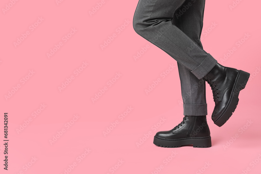 Legs of young woman in stylish black leather boots on pink background