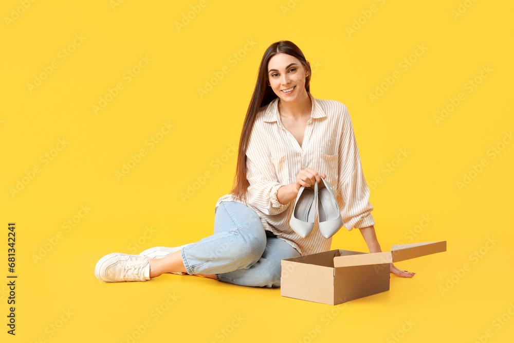 Beautiful young woman in stylish white sneakers and cardboard box with high heels on yellow background