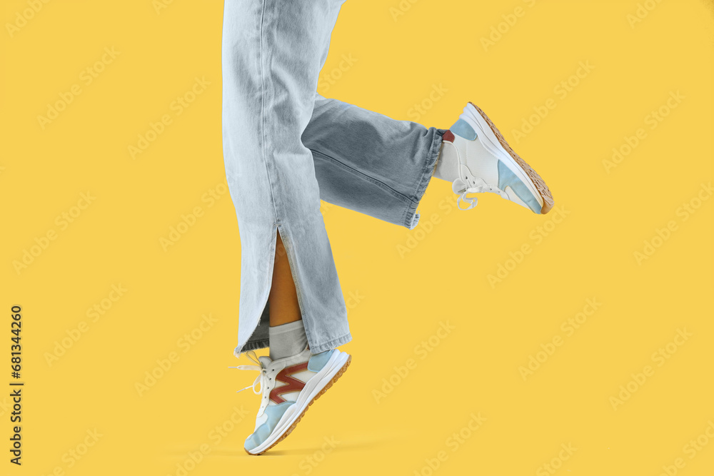 Female legs in stylish sneakers on yellow background