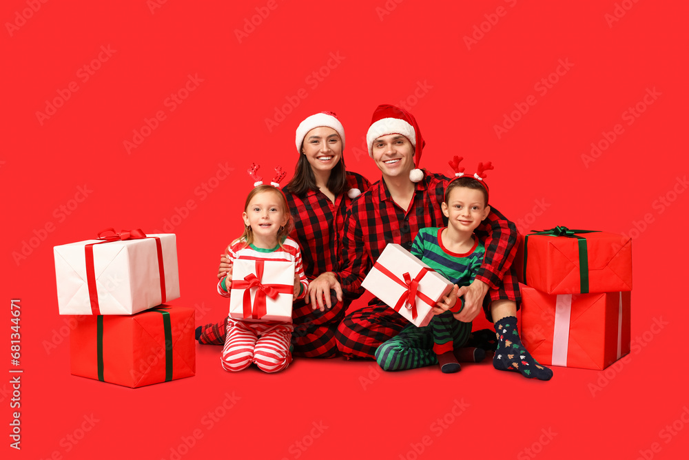 Happy family in pajamas with Christmas gifts on red background