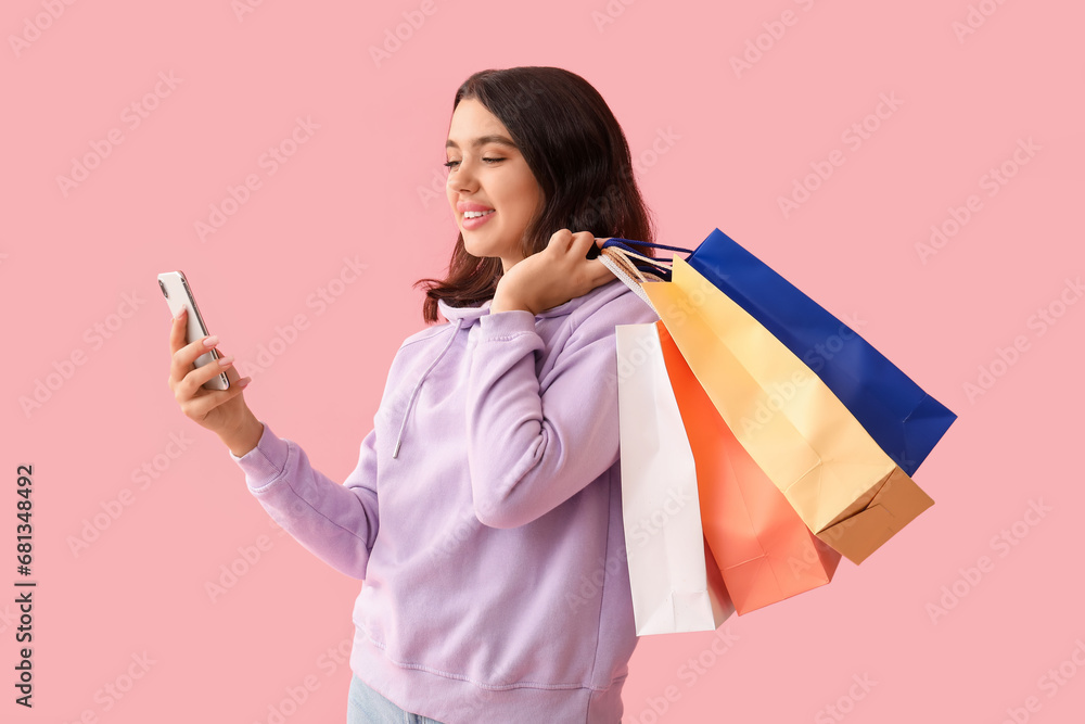 Young woman with mobile phone and shopping bags on pink background