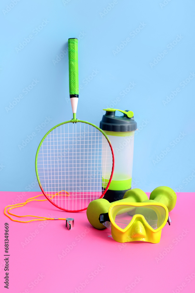 Badminton racket with dumbbells, swimming goggles and sports bottle on colorful background