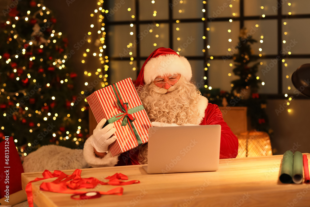 Santa Claus with laptop and Christmas gift at home