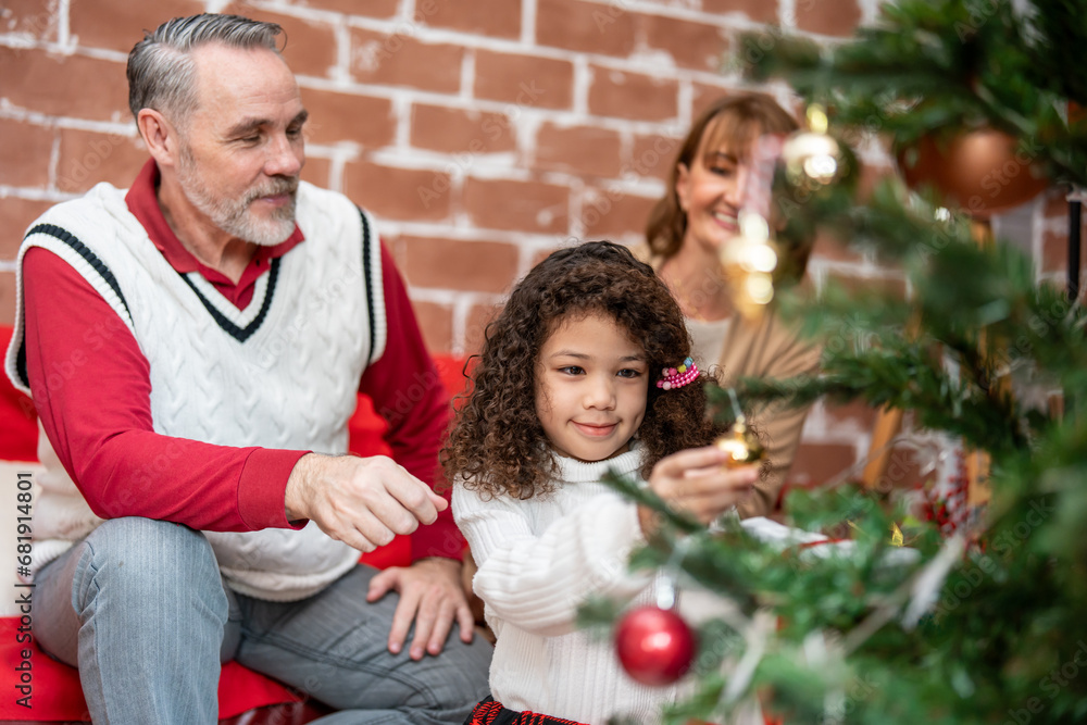 Caucasian family and young daughter decorate Christmas tree in house. 