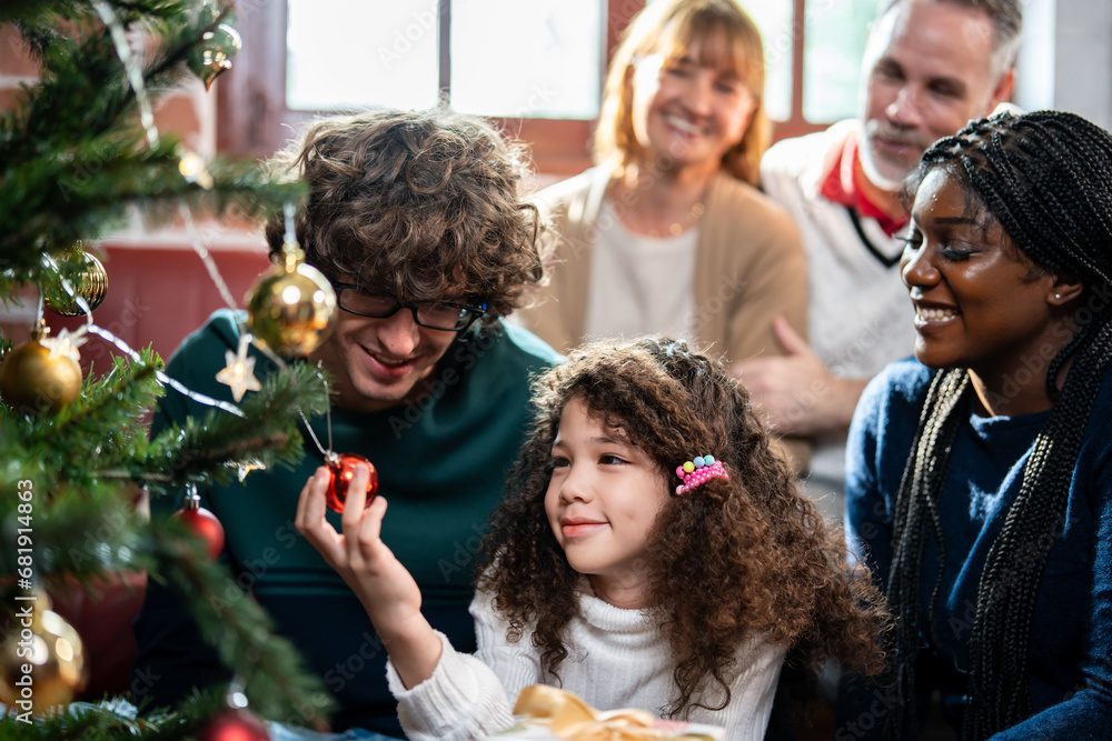 Multi-ethnic family and young daughter decorate Christmas tree in house. 